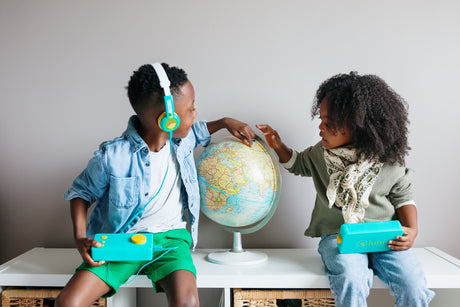 Deux enfants avec leur conteuse Lunii autour d’un globe terrestre